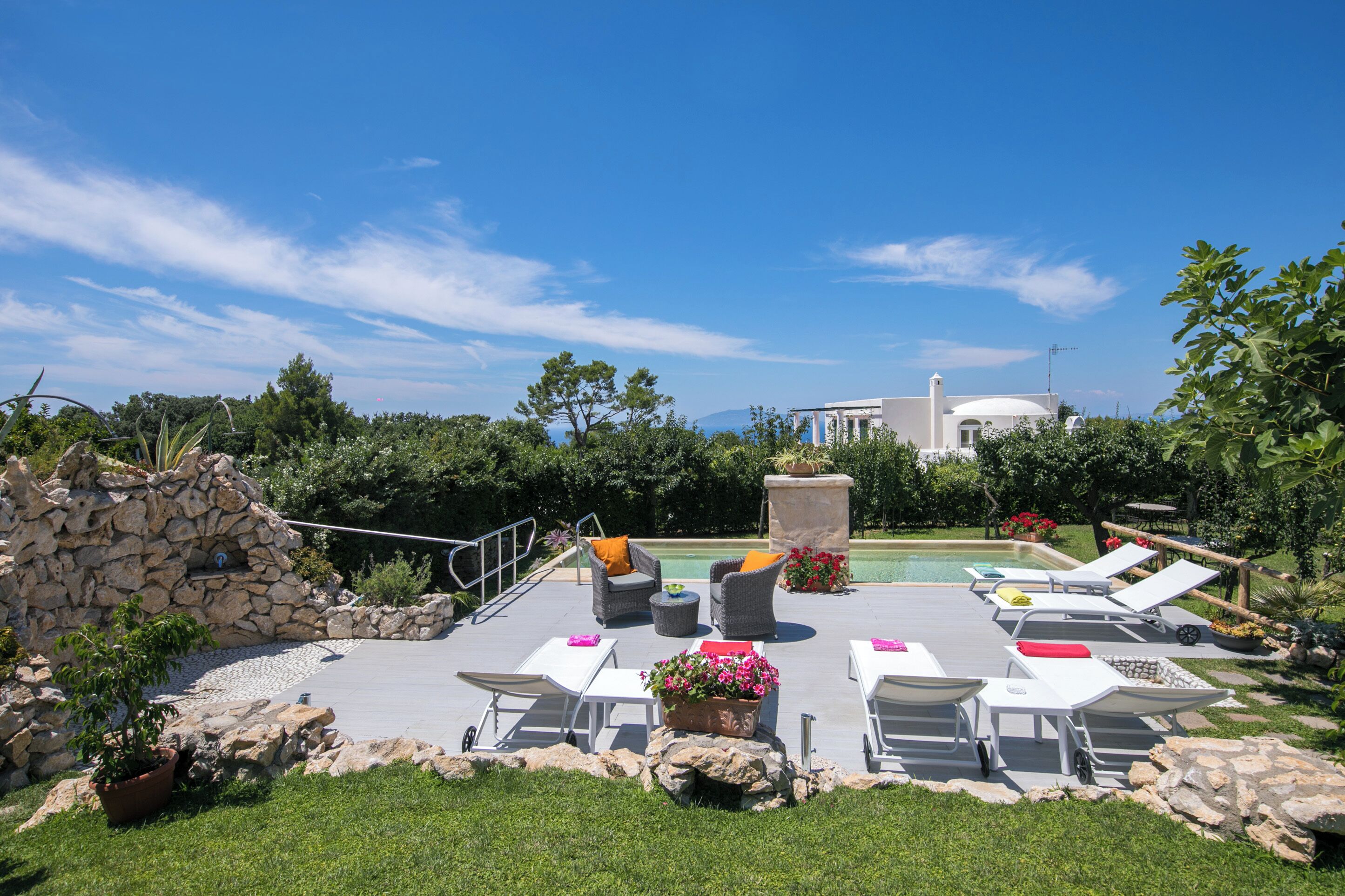 Un área de piscina al aire libre con sillones de descanso, un muro de piedra y una vista de un edificio con cúpula al fondo.