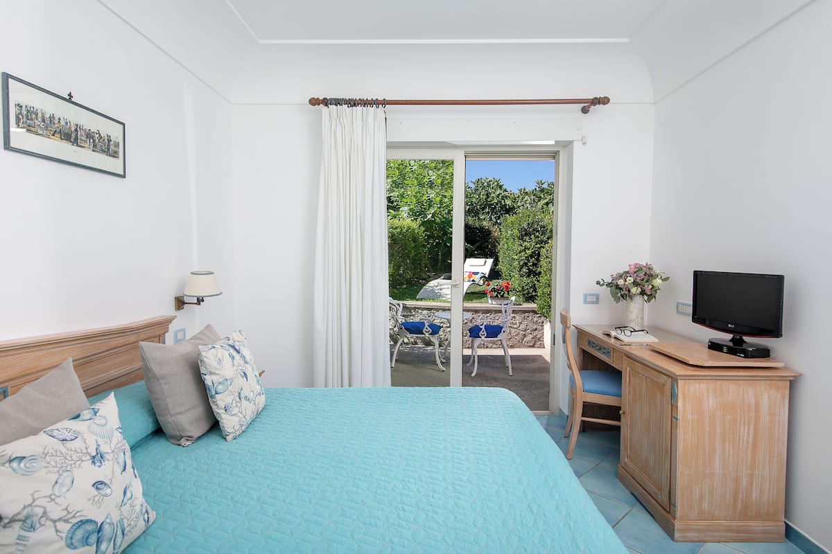 A bedroom with a bed, a desk, a television, and a view of the outdoors.