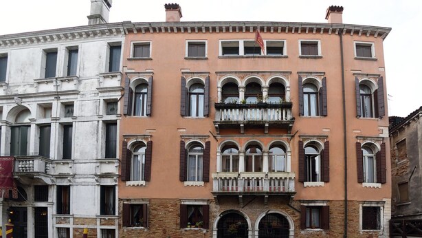 Un edificio histórico con múltiples ventanas y un balcón central, junto a un canal con barcos.
