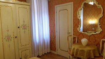 A room with a white door, a mirror with an ornate frame, a table with a vase, and floral-decorated cabinets.