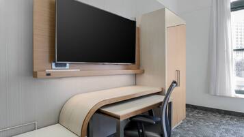 A modern office space with a built-in desk, a mounted TV, and a view of the city through a window.