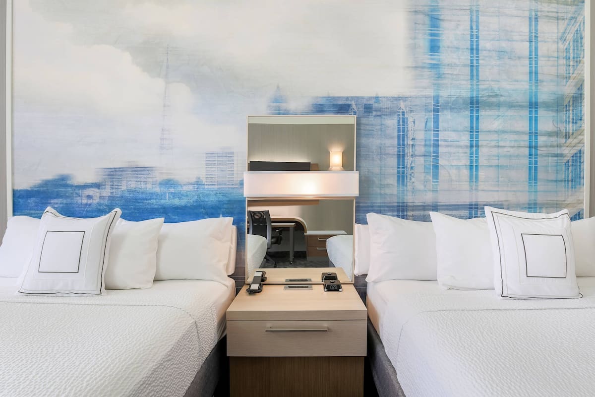 A hotel room with two beds, a desk, and a mirror.
