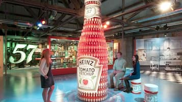 Uma grande escultura de garrafa de ketchup Heinz em um espaço interno moderno, com tetos aparentes e elementos industriais.