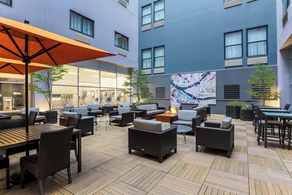 A modern outdoor seating area with wicker furniture, a wooden floor, and a large map mural on the building wall.