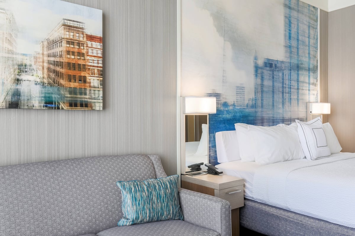 A hotel room with a bed, a sofa, a nightstand, and a painting of a cityscape.