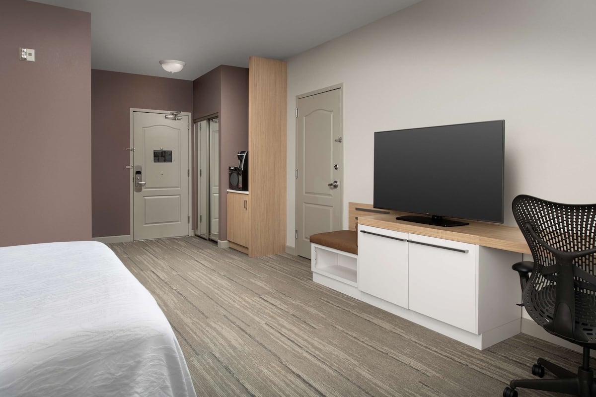 Une chambre d’hôtel comprenant un lit, un bureau avec une télévision, une chaise et une petite kitchenette.