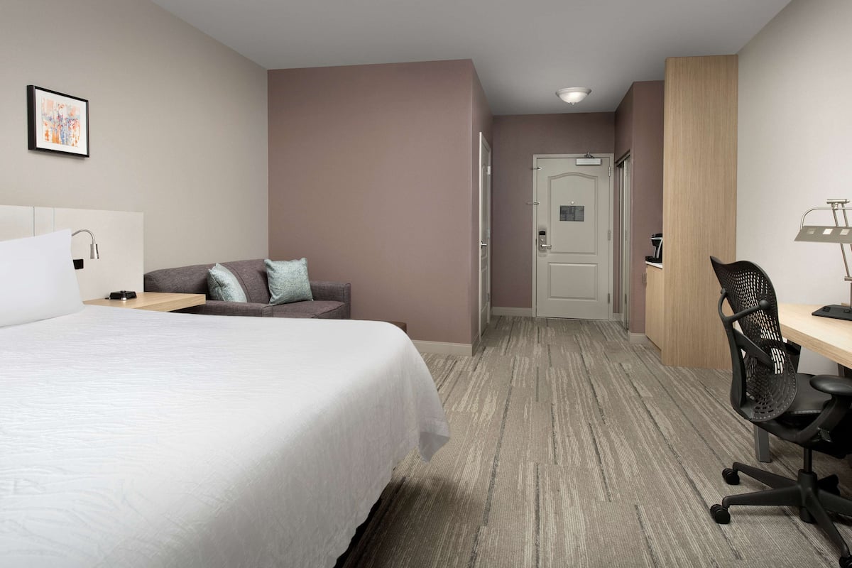 Une chambre d’hôtel comprenant un lit, un bureau, une chaise, un canapé et une porte donnant sur une autre pièce.