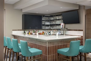 A bar area with a tiled backsplash, a flat-screen TV mounted above the bar, and teal bar stools.