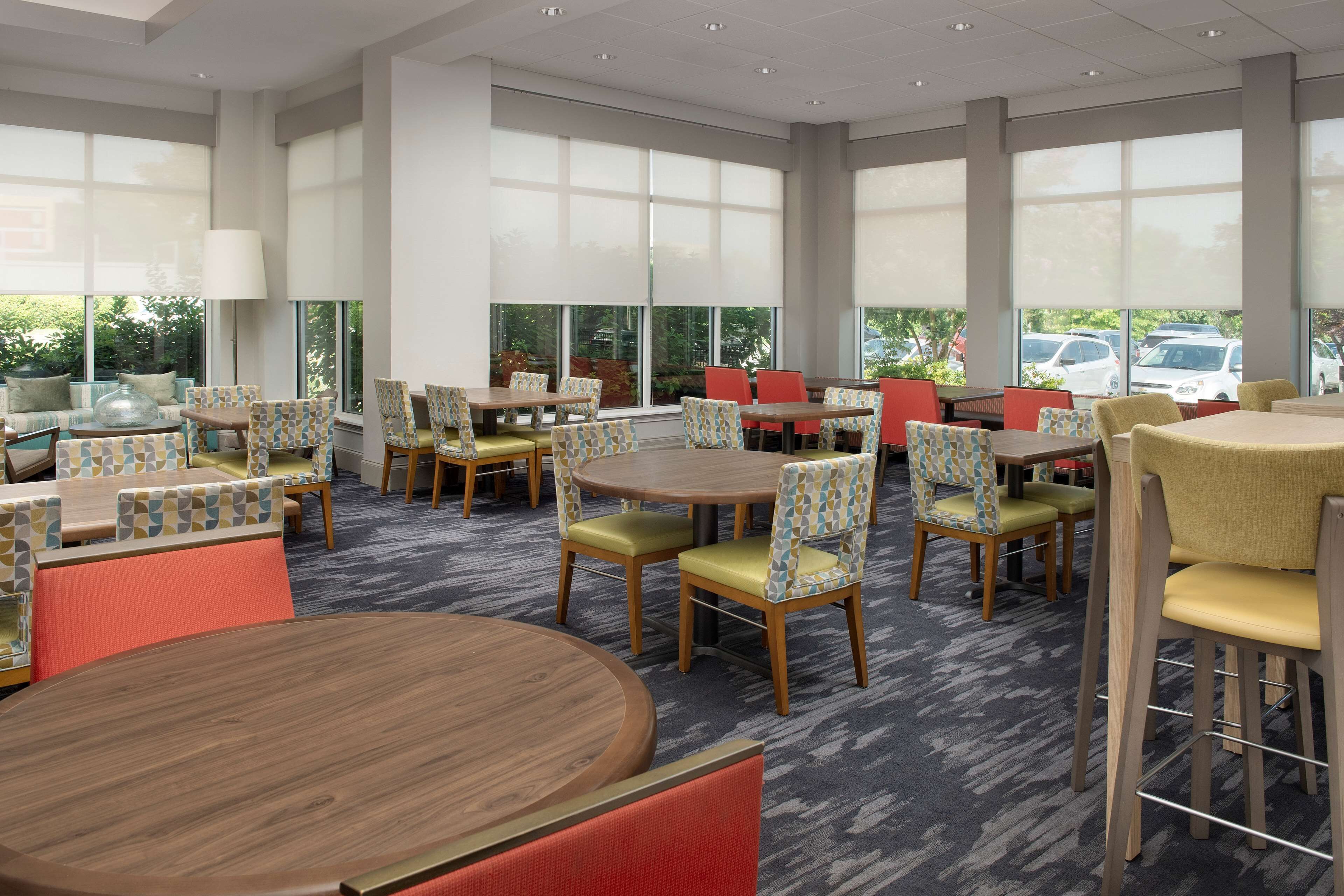 A spacious indoor area with multiple round tables and chairs, large windows, and a carpeted floor.