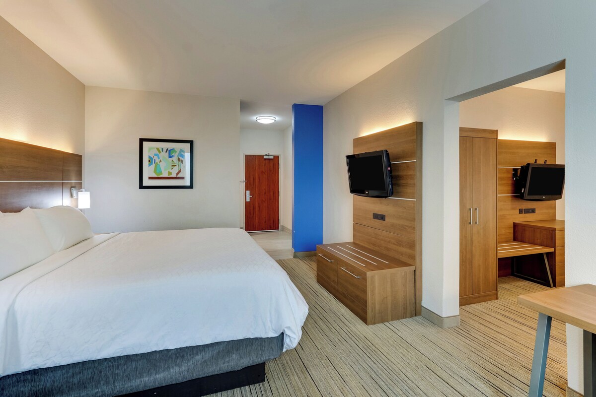 Una habitación de hotel moderna con una cama grande, un armario de madera, un televisor y un escritorio.