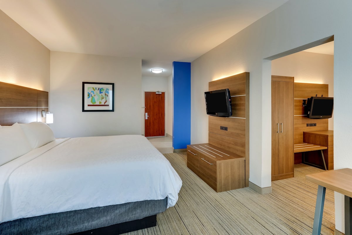Una habitación de hotel moderna con una cama grande, un armario de madera, un televisor y un escritorio.