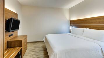 A hotel room with a bed, a wooden nightstand, a television, and a wall-mounted light.