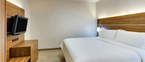 A hotel room with a bed, a wooden nightstand, a television, and a wall-mounted light.