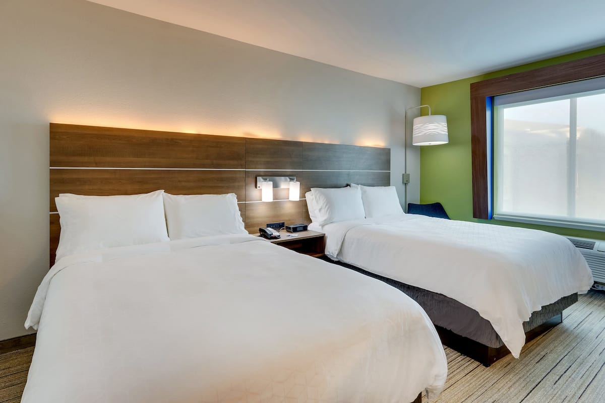 Habitación de hotel con dos camas, una mesita de noche, una lámpara y un ventanal grande.
