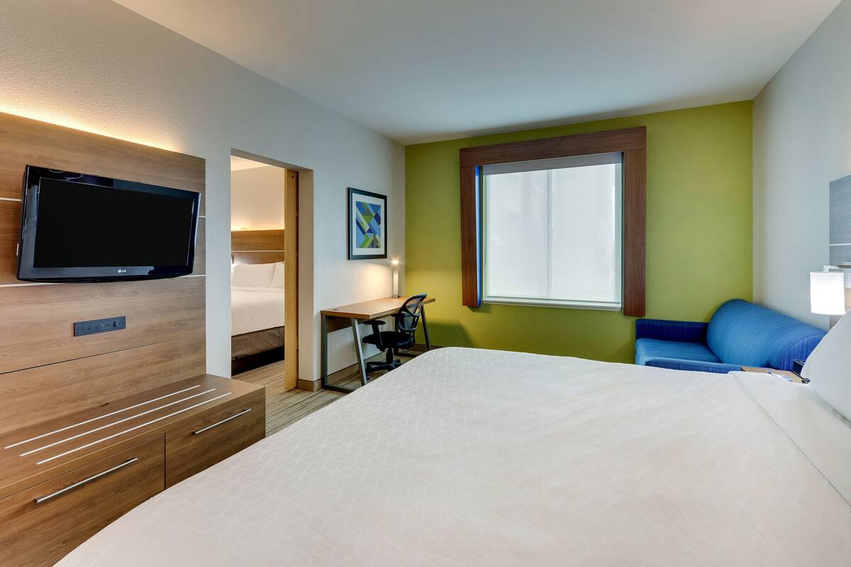 Habitación de hotel con cama, escritorio con silla, televisor y ventana con cortinas.