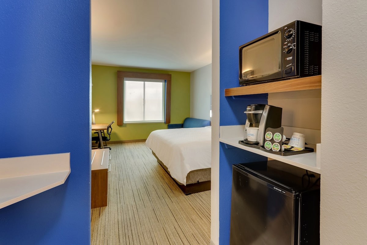 Una habitación de hotel con cama, microondas, cafetera y refrigerador.