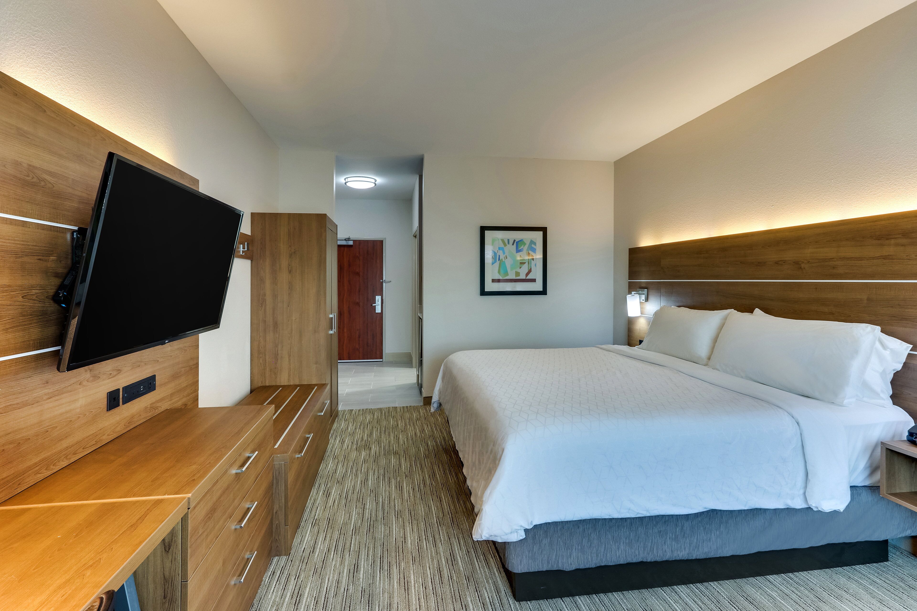Une chambre d’hôtel avec un lit, un téléviseur fixé au mur, une armoire en bois et une porte donnant sur une autre pièce.