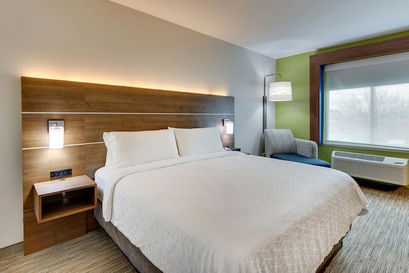 Moderni hotellihuone, jossa on suuri sänky, yöpöytälamput, yöpöytä, ikkuna, josta on näkymä, ja sisäänrakennettu ilmastointilaite.