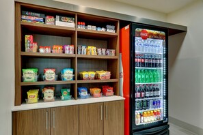 Una máquina expendedora repleta de Coca-Cola y otras bebidas, junto con estantes con snacks como Lay's y Doritos.