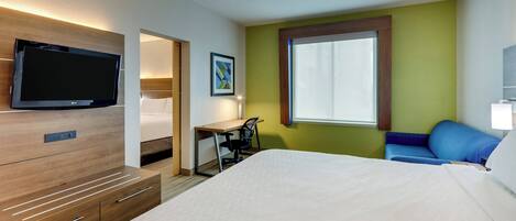 Una habitación de hotel con cama, escritorio, silla, televisor y ventana.