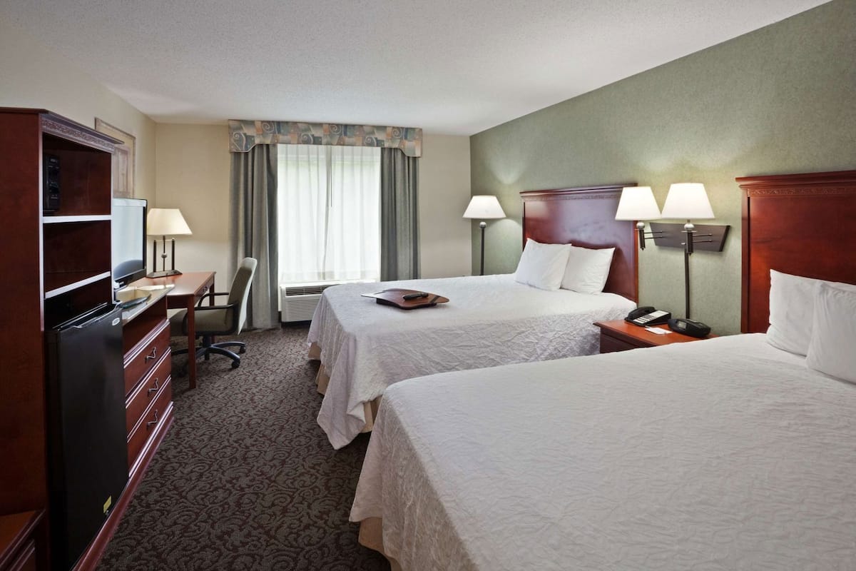 A hotel room with two beds, a desk, a chair, a television, and a minibar.