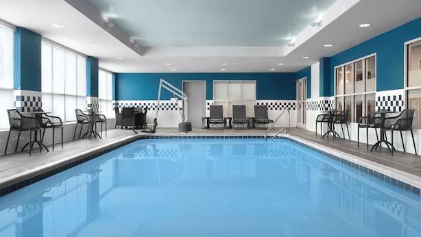 A modern indoor pool with clear blue water, surrounded by black metal chairs and tables.