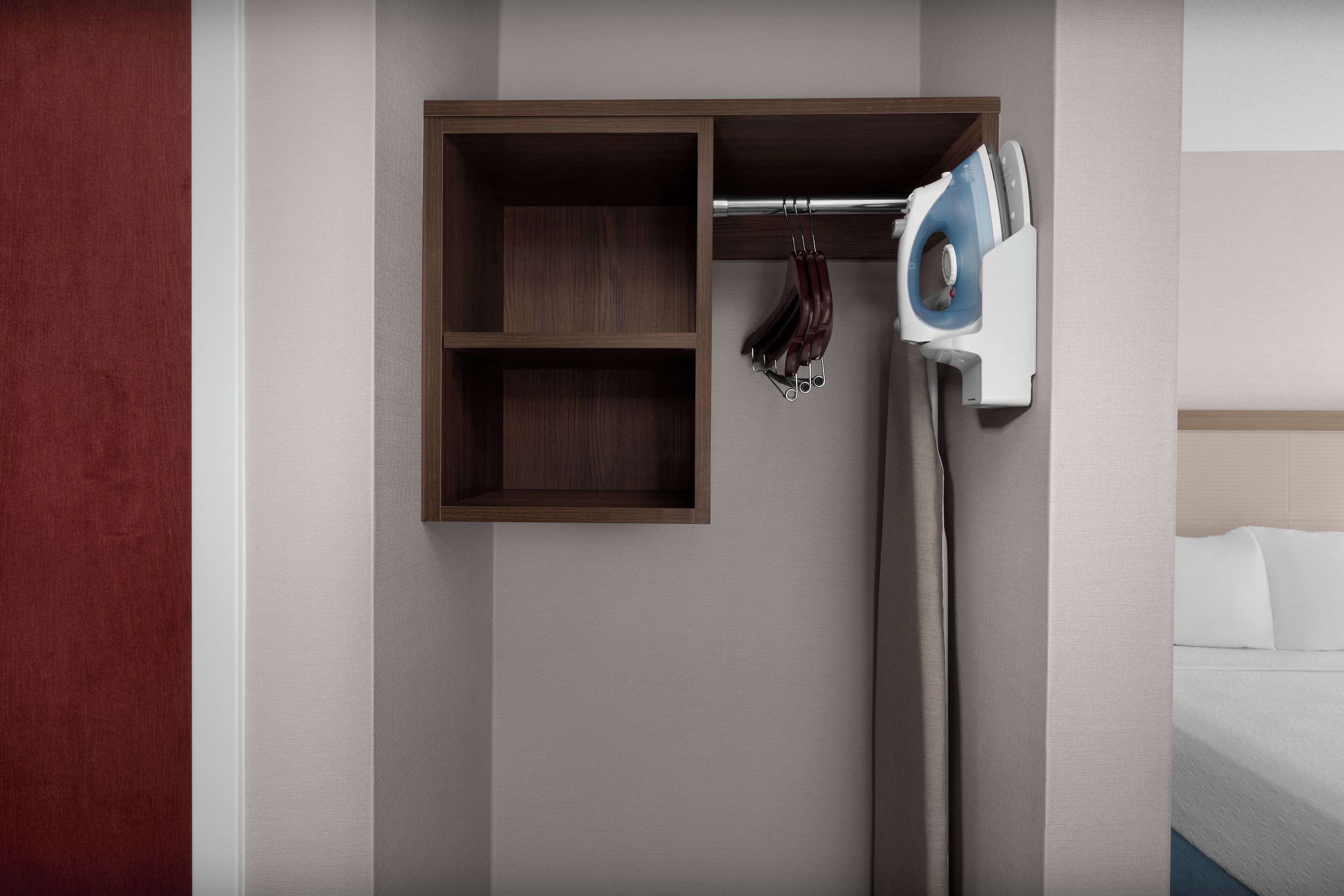 A hotel room with a wooden shelf unit, an iron, and a bed.
