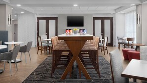 A modern conference room with a central table, multiple chairs, and a flat-screen TV on the wall.