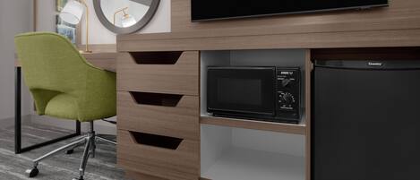 Une chambre d’hôtel moderne équipée d’une télévision à écran plat, d’un four à micro-ondes, d’un réfrigérateur, d’un fauteuil vert et d’un bureau avec des tiroirs.