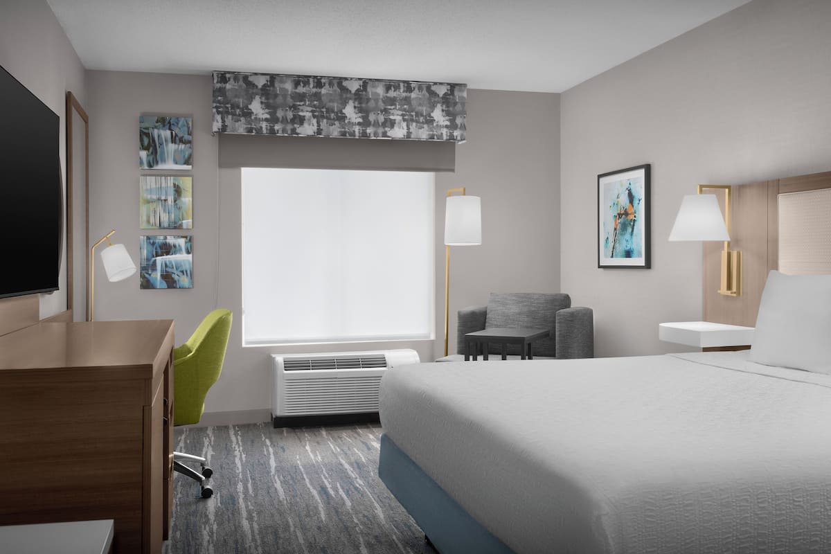 A hotel room with a bed, desk, chair, and artwork on the walls.