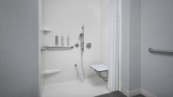 A modern bathroom with a walk-in shower, grab bars, and a white towel rack.