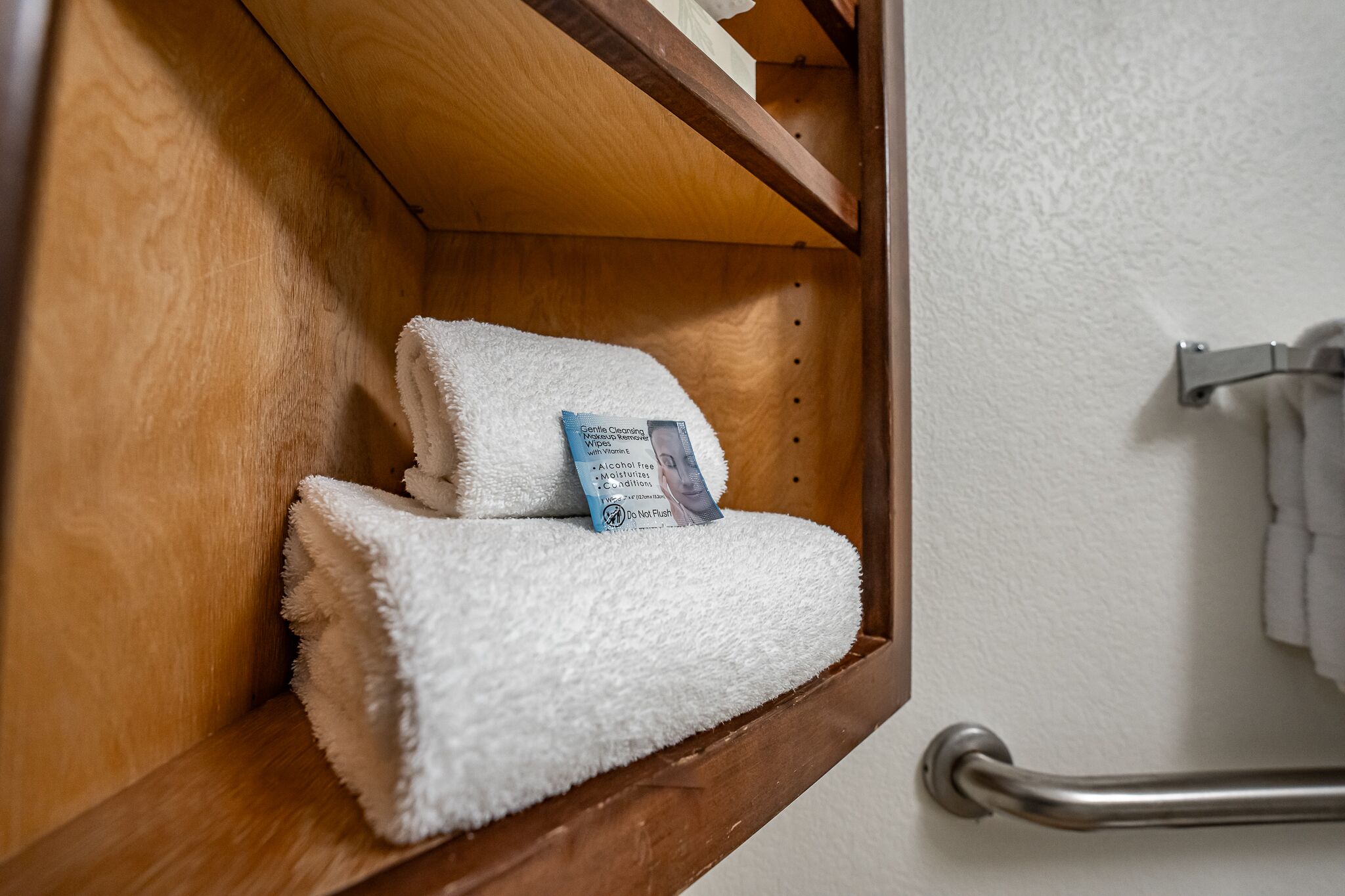A wooden shelf with a white towel and a packet of Gentle Cleansing Wipes.
