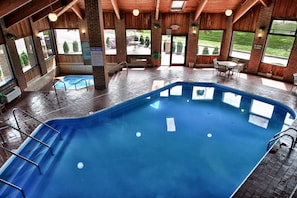 A large indoor swimming pool with clear pool rules and a view of the outdoors through large windows.