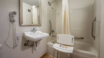 Un baño con lavamanos, espejo, secador de pelo, ducha y un banco accesible para sillas de ruedas.