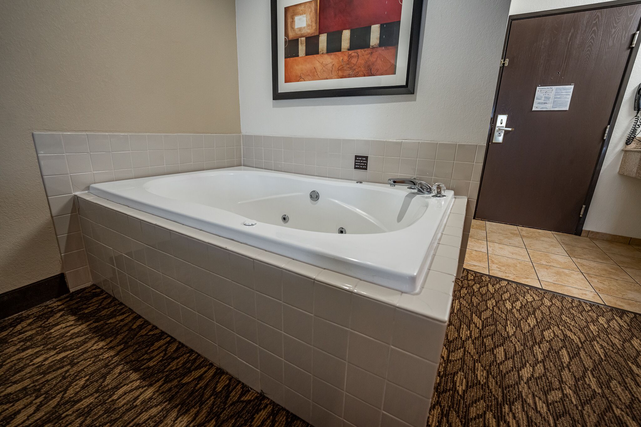 Una bañera grande y rectangular con revestimiento blanco, piso de baldosas y una puerta marrón con un letrero.