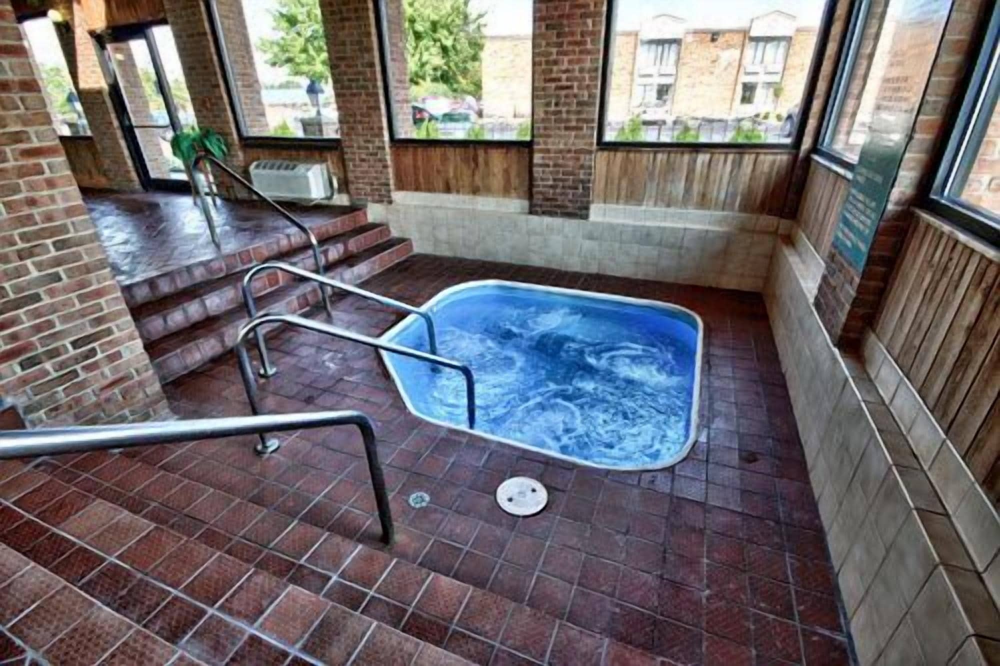 Uma área de spa com hidromassagem, degraus de acesso e vista para o exterior através de grandes janelas.