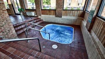 Uma área de spa com hidromassagem, degraus de acesso e vista para o exterior através de grandes janelas.