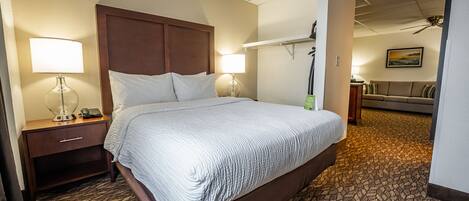 A hotel room with a large bed, two bedside tables with lamps, a nightstand, a sofa, and a painting on the wall.