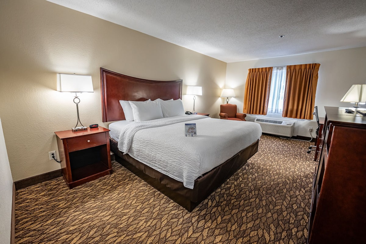 Quarto de hotel com uma cama grande, duas mesas de cabeceira com luminárias, um aquecedor e uma janela com cortinas.