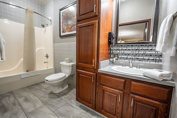 A bathroom with a bathtub, toilet, and wooden vanity with a sink and mirror.