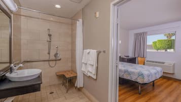 A bathroom with a sink, shower, and a small stool. There is a towel rack with towels and a window with curtains.