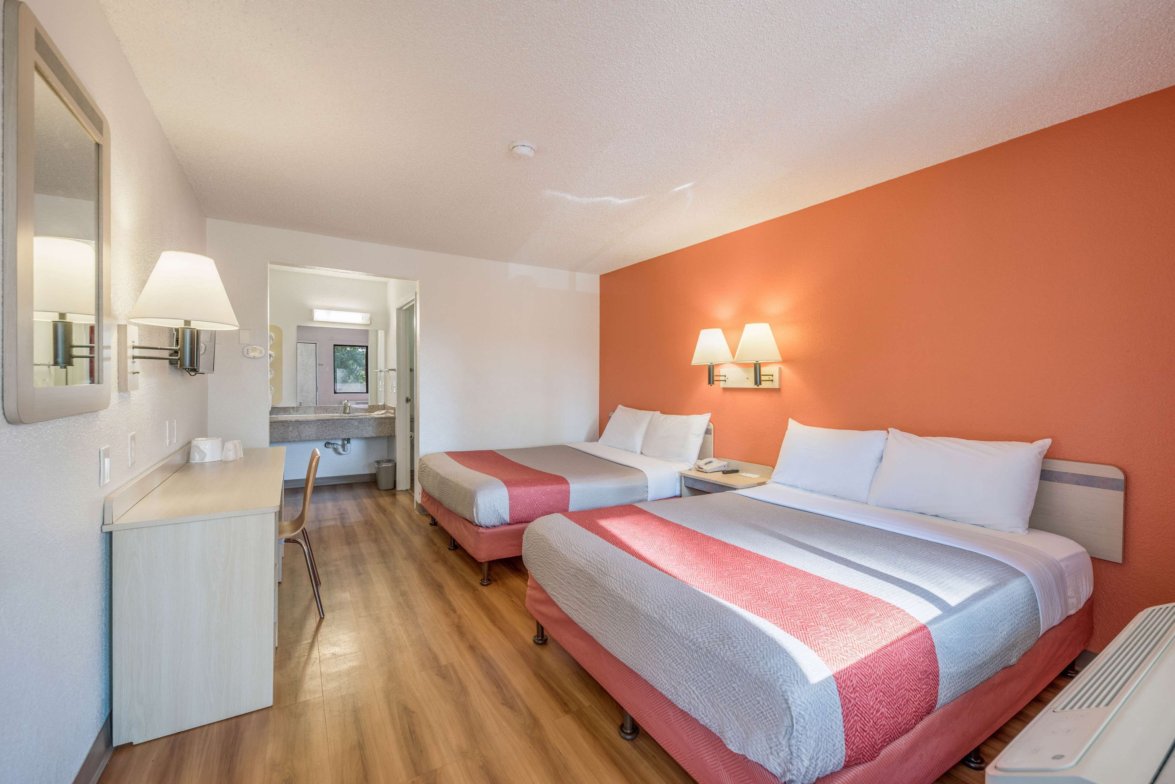 Una habitación de hotel con dos camas, un escritorio y un espejo.