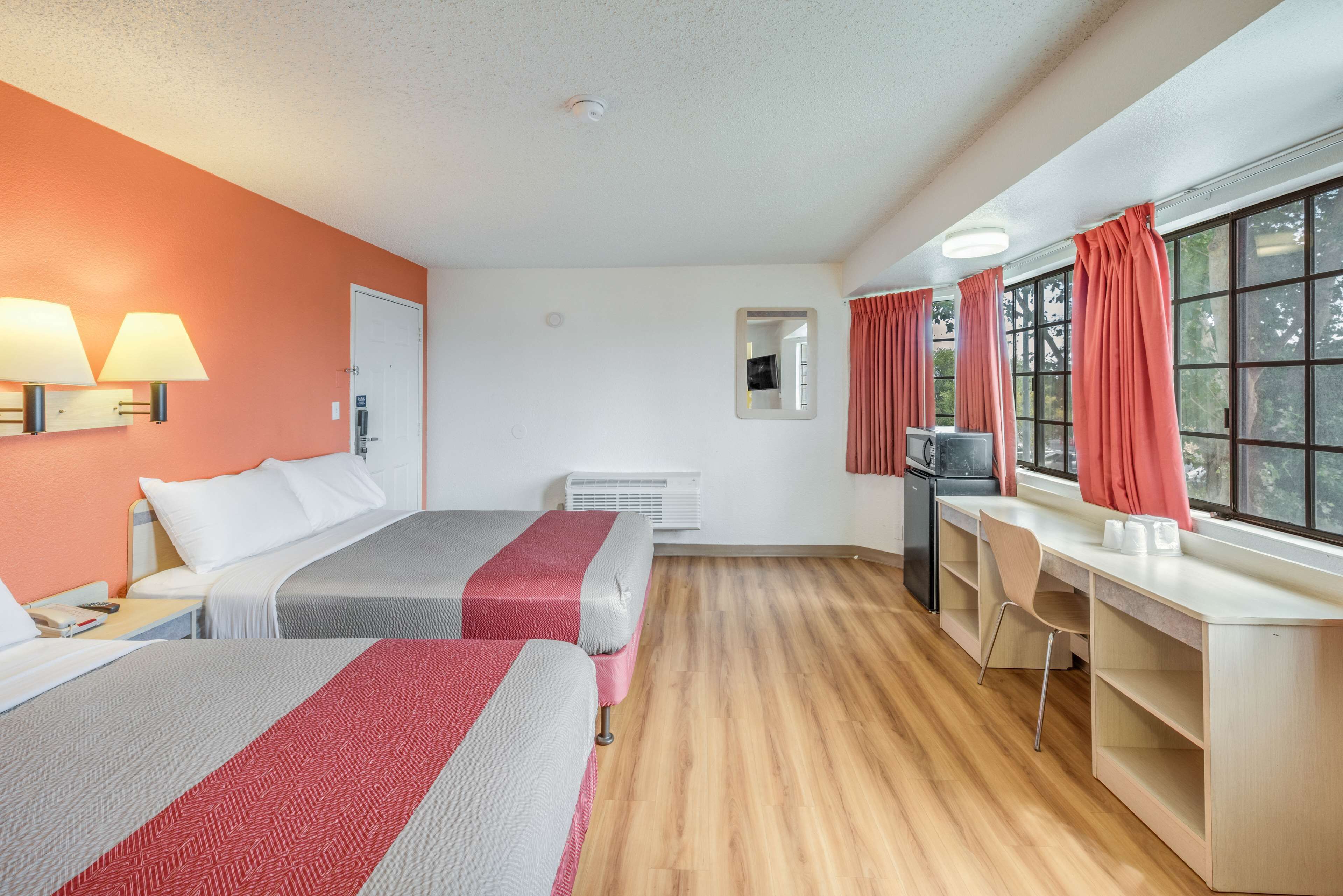 A hotel room with two beds, a desk, a chair, a TV, and a window with curtains.