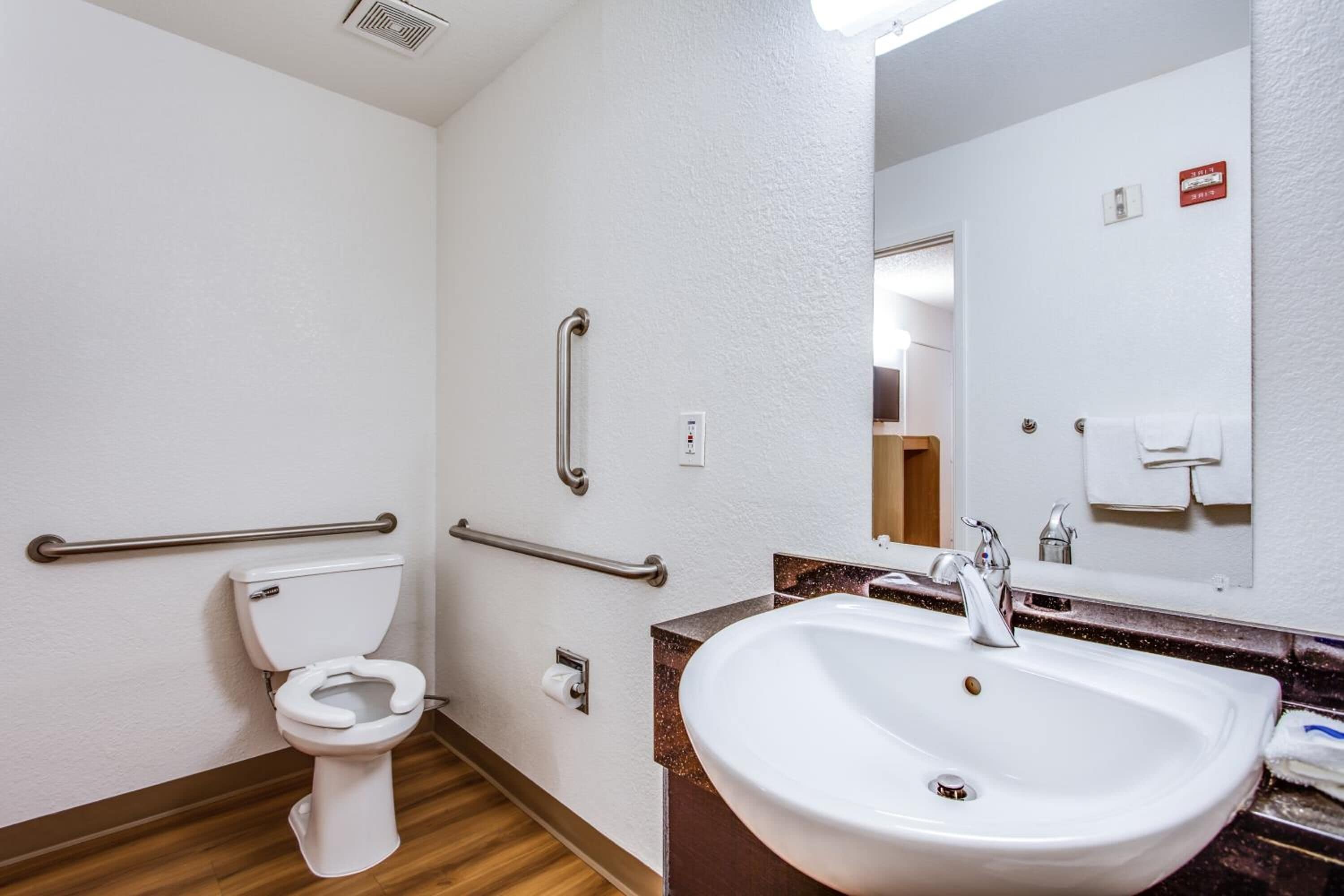 Een badkamer met een wit toilet, een wastafel met spiegel en handgrepen.