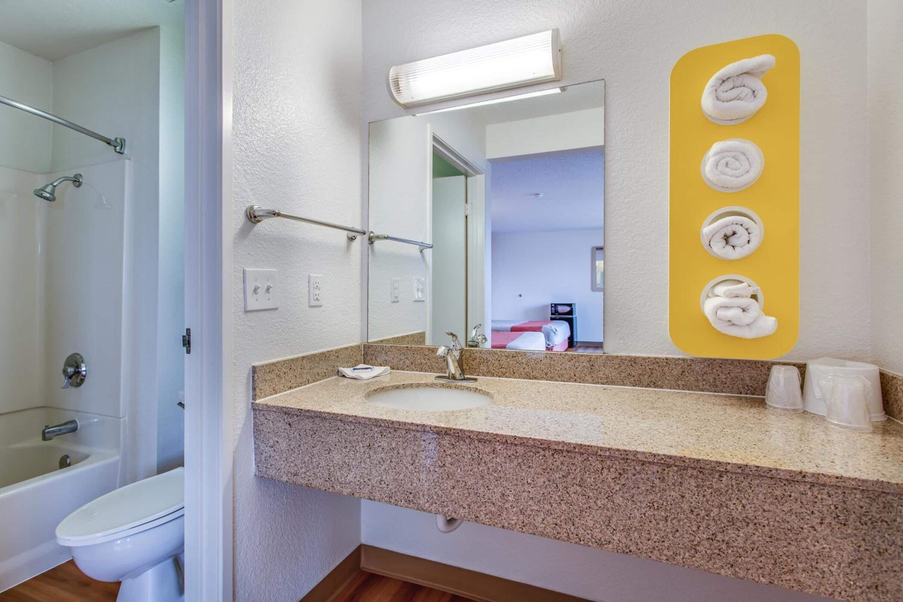 Une salle de bain équipée d’un lavabo, d’un miroir, d’un distributeur de serviettes et d’un espace douche.