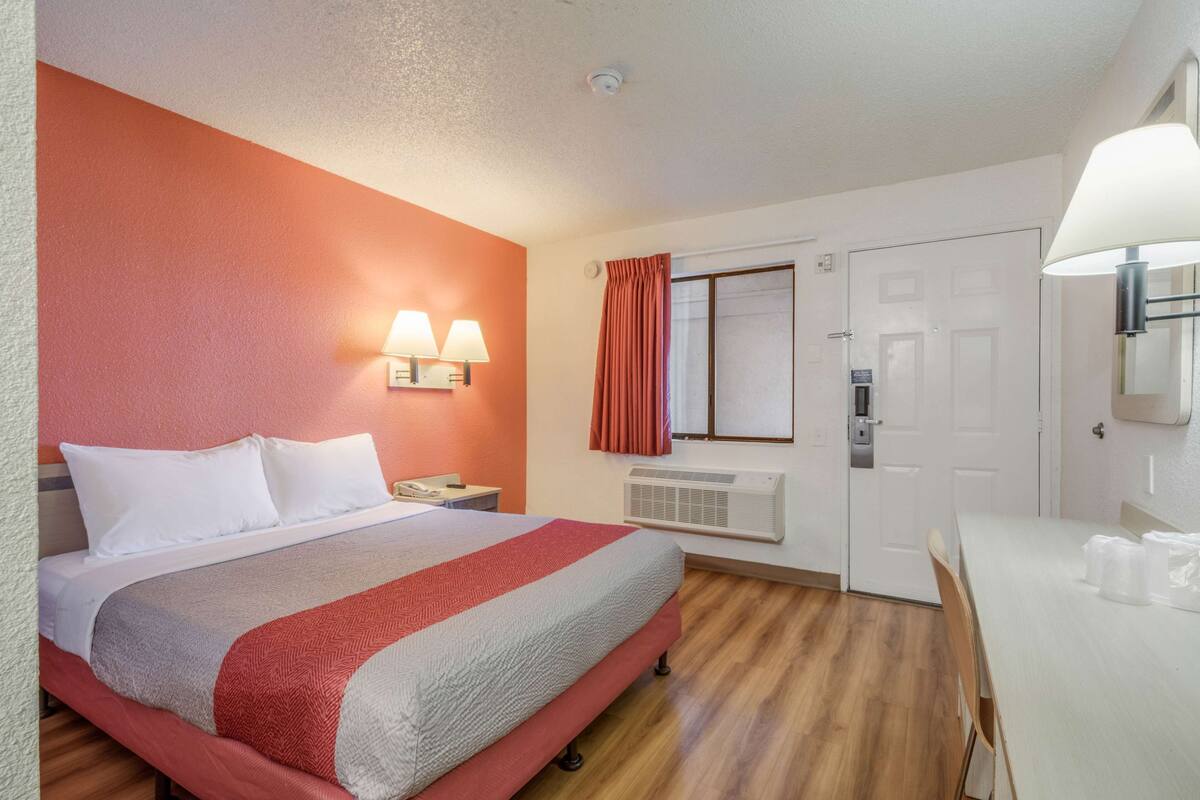 A hotel room with a bed, bedside lamps, a desk, and a window with curtains.