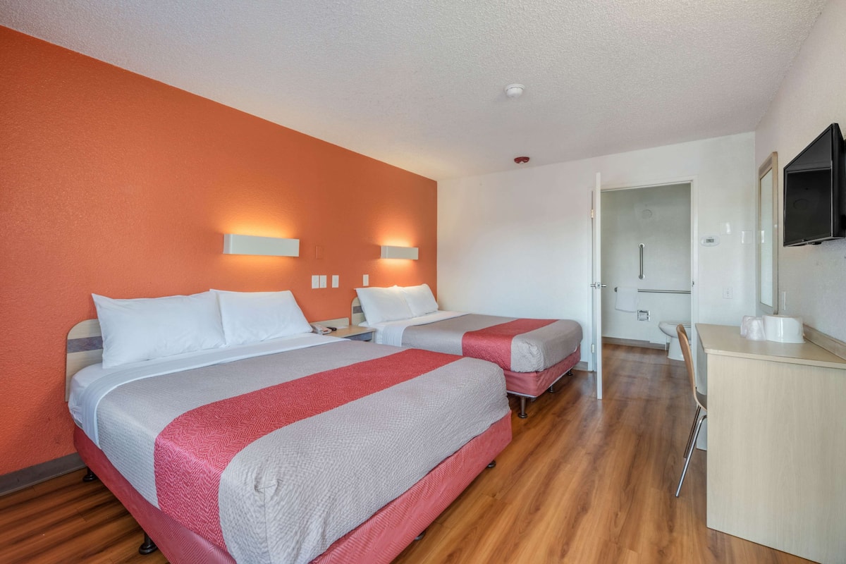 A hotel room with two beds, a desk, a chair, and a television.