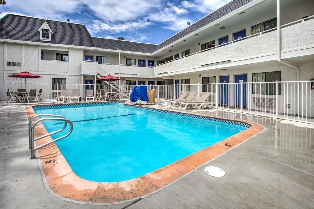 A swimming pool with lounge chairs and umbrellas, surrounded by a building with multiple balconies and doors.
