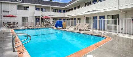 A swimming pool with lounge chairs and umbrellas, surrounded by a building with multiple balconies and doors.