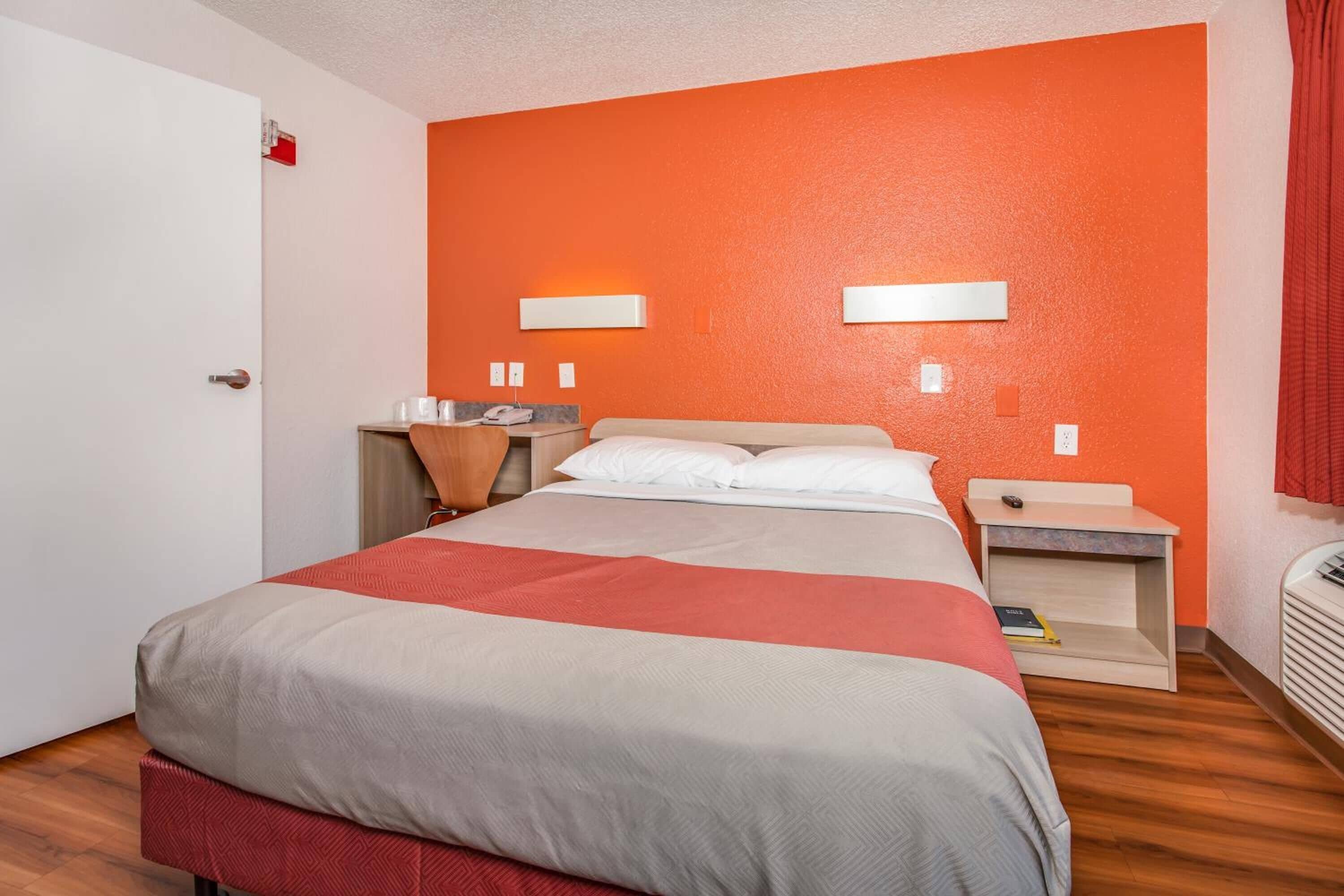 Une chambre d’hôtel avec un lit, des tables de chevet, un bureau et un mur d’accent de couleur rouge-orangée.